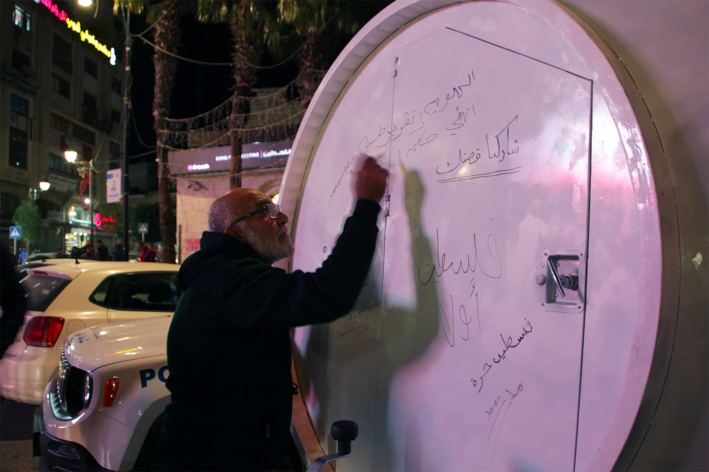 A person writes on a circular translucent surface illuminated in pink.